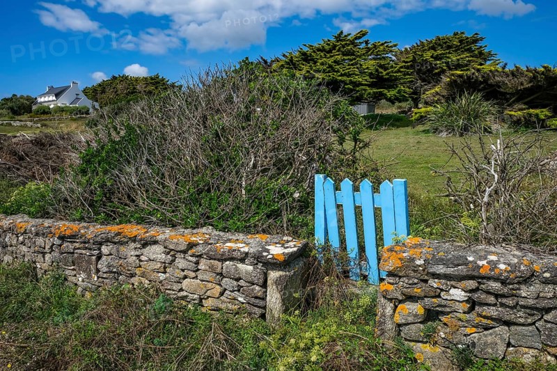 Pors Poulhan, Brittany, France - Picturesque dry stone wall with blue garden gate on the GR36 coastal footpath. A house at the back