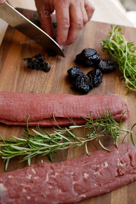 Swabian cuisine, preparation of lamb with prunes, raw lamb, rosemary, herbs, sliced garlic, lemon zest, fillets on wooden board, cutting prunes, kitchen knife, grandmother's kitchen, regional, home cooking, typical Swabian, traditional cuisine reinterpreted, food photography, man's hand, studio, Germany, Europe