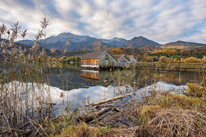 Boathouses in the lake at sunrise, Lake Kochel in autumn with reflection, behind mountain peaks Herzogstand and Heimgarten Upper Bavaria, Bavaria, Germany, Europe