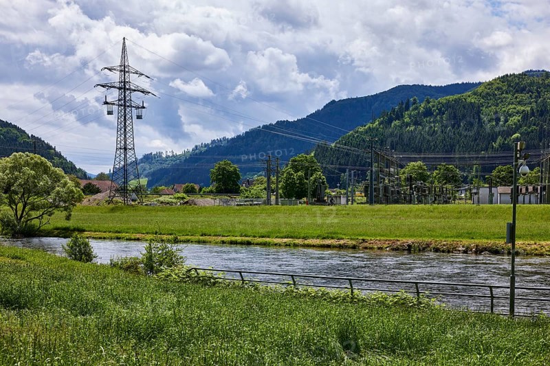 River Kinzig, bank with meadow and trees, electricity pylon, transformer station, hilly landscape with coniferous forest, overcast sky with Nimbostratus clouds, sunlight, Hausach, Black Forest, Ortenaukreis, Baden-Württemberg, Germany, Europe