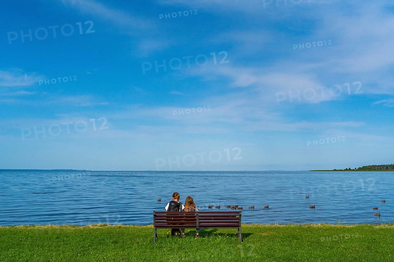 Woman and girl sitting on a bench in a meadow on the shore of the Szczecin Lagoon in the village of Altwarp, Naturpark Am Stettiner Haff, Mecklenburg-Vorpommern, Germany, Europe
