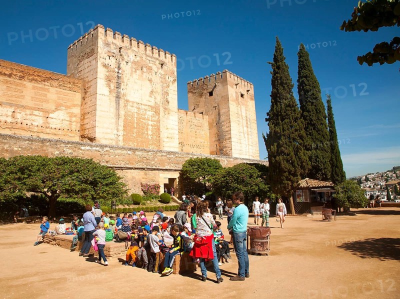 Children on a school trip sitting outside the fortified castle walls of the historic Alcazaba, of the Alhambra, Granada, Spain, Europe