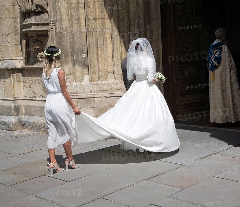 Bride wearing white wedding dress with her bridesmaid as they enter Bath Abbey church, Bath, Somerset, England, United Kingdom, Europe