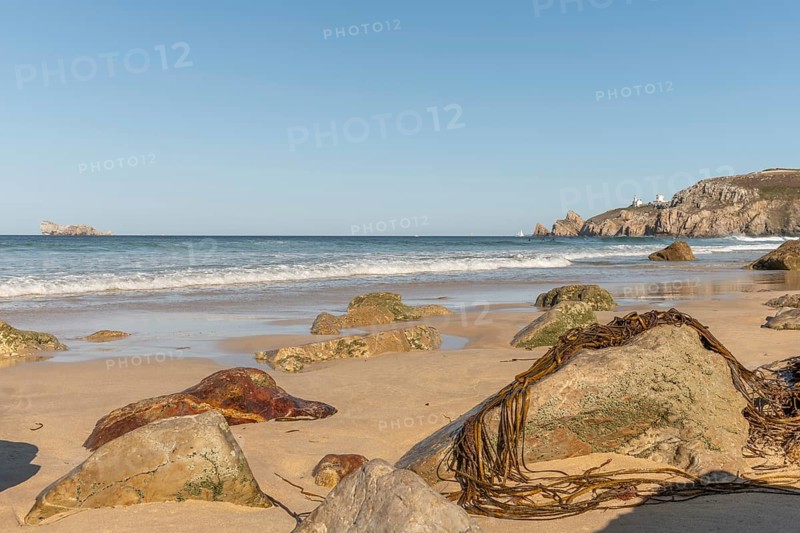 A rocky beach with a large rock in the foreground and a boat in the distance. The beach is quiet and peaceful, with the water. Camaret sur mer, Crozon, Finistere, Brittany, France, Europe