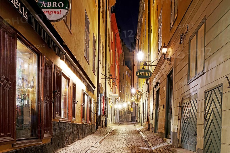 Narrow cobblestones with illuminated shop windows and historic buildings in the evening, winter, Gamla Stan, Old Town, Stockholm Sweden