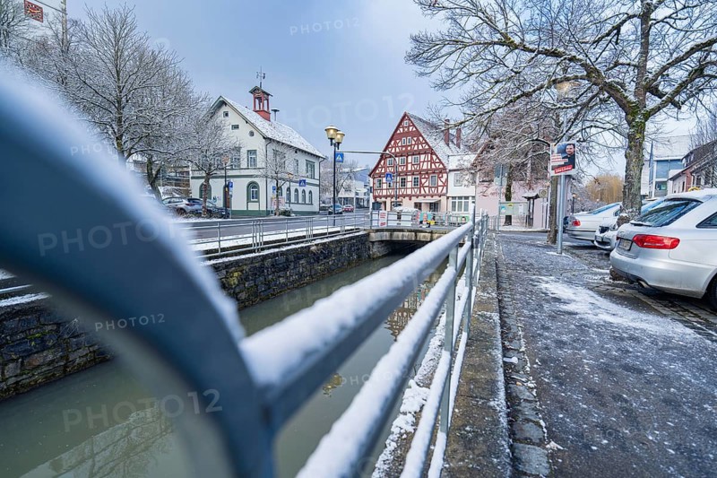 Road with snow cover next to river, view of half-timbered houses and bridge in wintry cityscape, Aidlingen, Böblingen district, Germany, Europe