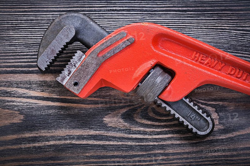 Adjustable monkey wrench on wooden board directly above plumbing concept