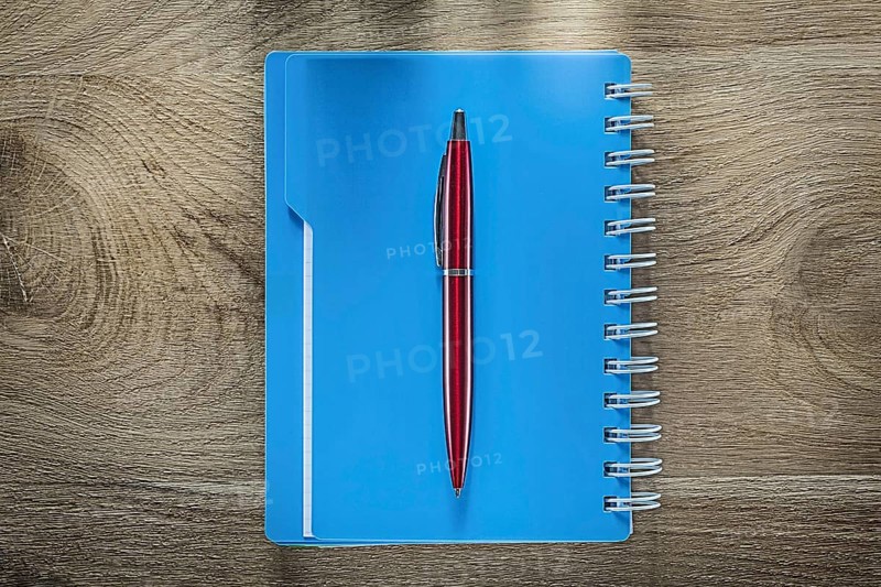 Biro pen spiral copybook on wooden board