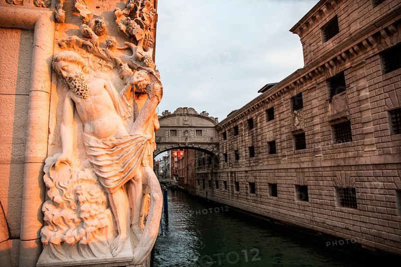 Morning light falls on a stone sculpture of an ancient deity, behind the Bridge of Sighs or Ponte dei Sospiri at the Doge's Palace over the Rio di Palazzo, Venice, Veneto, Italy, Europe