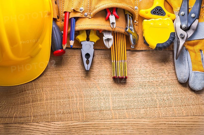 Aerial view construction tools in toolbelt hammer tapeline wrench nippers pliers cutter pencil screwdriver helmet on wooden board
