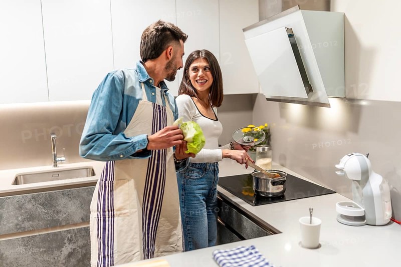 Happy couple wearing aprons, preparing healthy meal together in their modern kitchen, enjoying quality time and teamwork