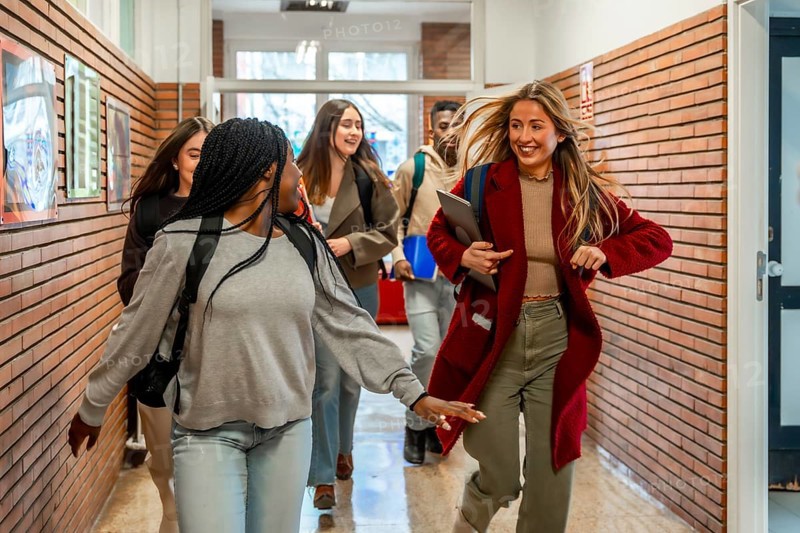 Cheerful diverse university students running joyfully through the school hallway after class, filled with energy and excitement for break time