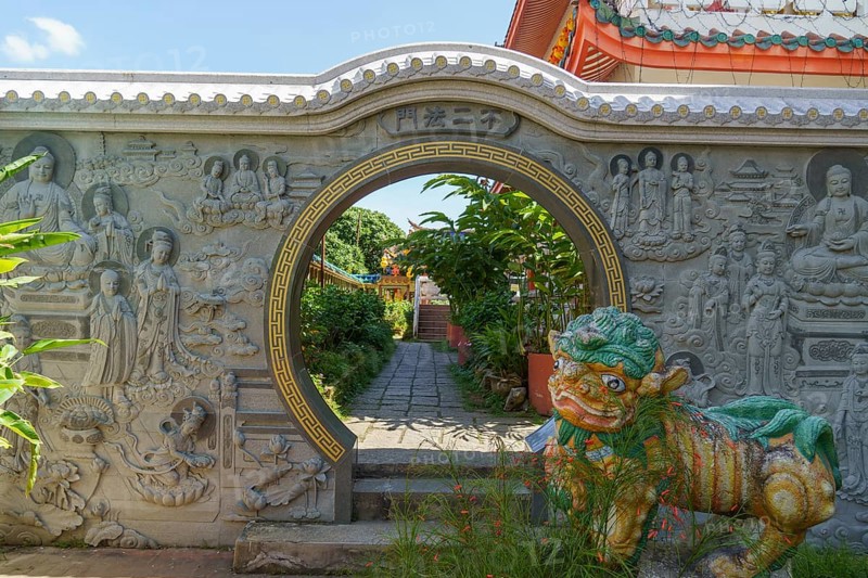 Entrance gate with stone reliefs and colourful figure. Leads to a well-kept garden path, penang, malaysia