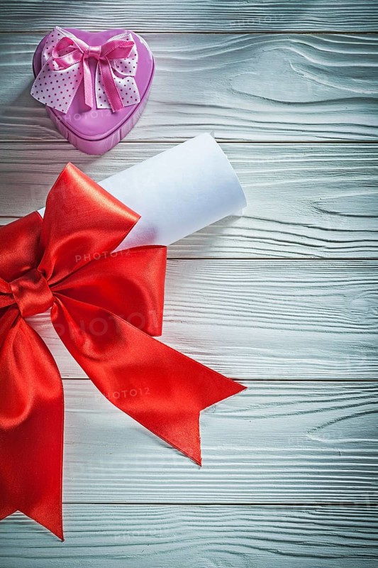 Paper roll with red bow metal present box on wooden board holidays concept