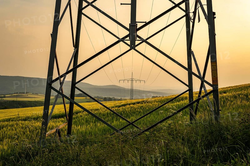 View through the struts of an electricity pylon to another electricity pylon in a wide landscape with fields and soft evening light, Großenberg, Lower Saxony, Germany, Europe