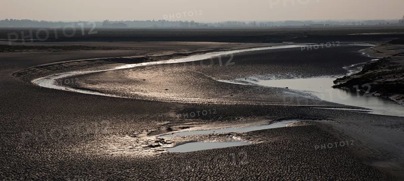 Mont-Saint-Michel, monastery hill, mudflats below the abbey at low tide, flood channel on the left, river Couesnon on the right