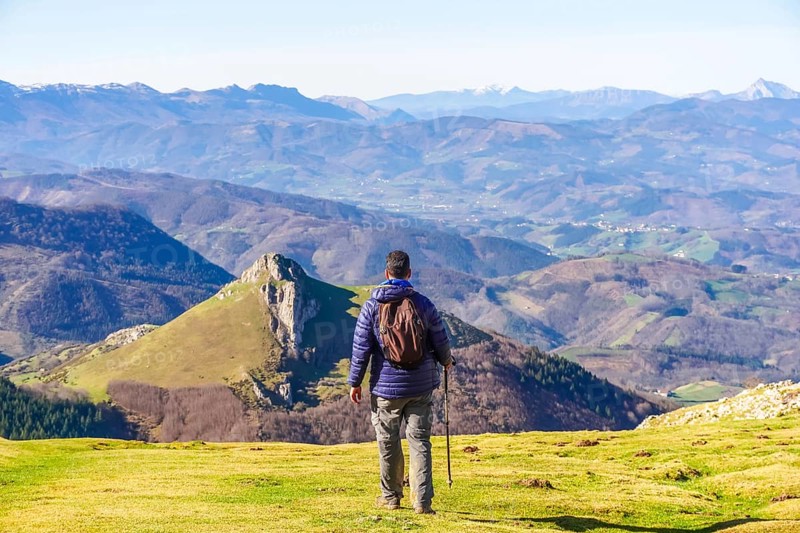Hiker with backpack and trekking poles enjoying breathtaking mountain view from mount txindoki in gipuzkoa, basque country, spain