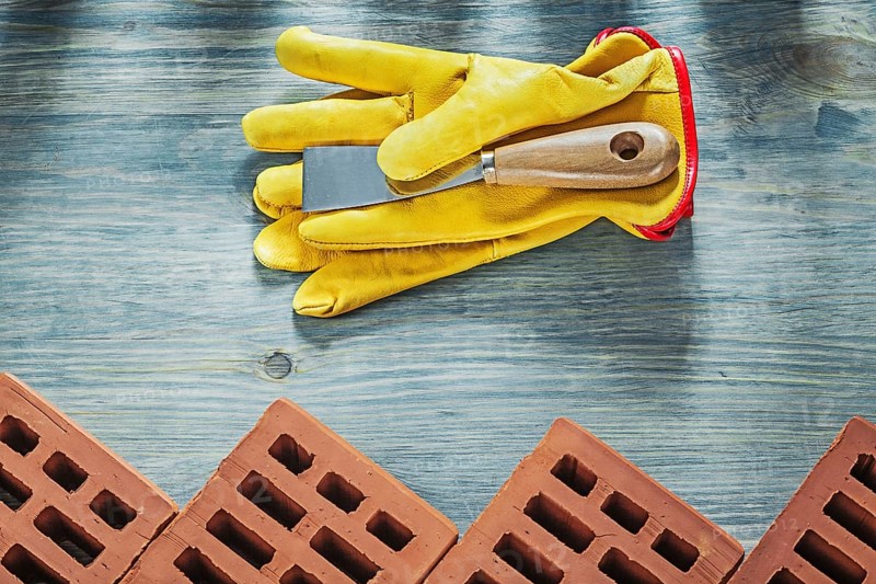Assortment of red construction bricks leather safety gloves palette knife building concept