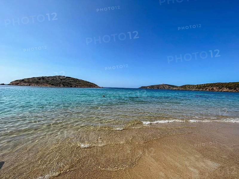 Calm beach with gentle waves and hills in the background under a blue sky, cagliari, sardinia, italy