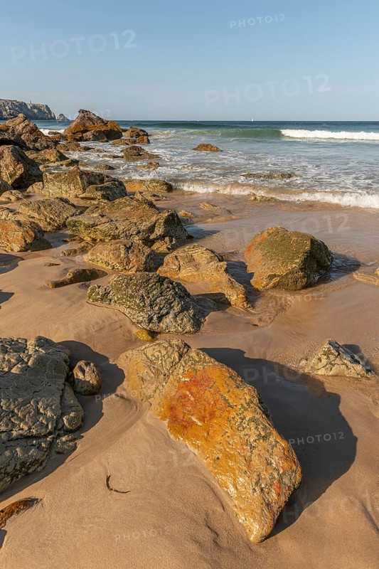 A rocky beach with a large rock in the foreground and a boat in the distance. The beach is quiet and peaceful, with the water. Camaret sur mer, Crozon, Finistere, Brittany, France, Europe