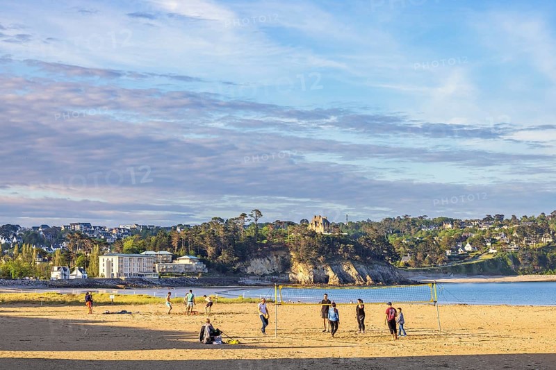 Young people playing beach volleyball on a sandy beach by the sea by a coastal village on the French coast, Morgat, Crozon peninsula, Bretagne, France, Europe