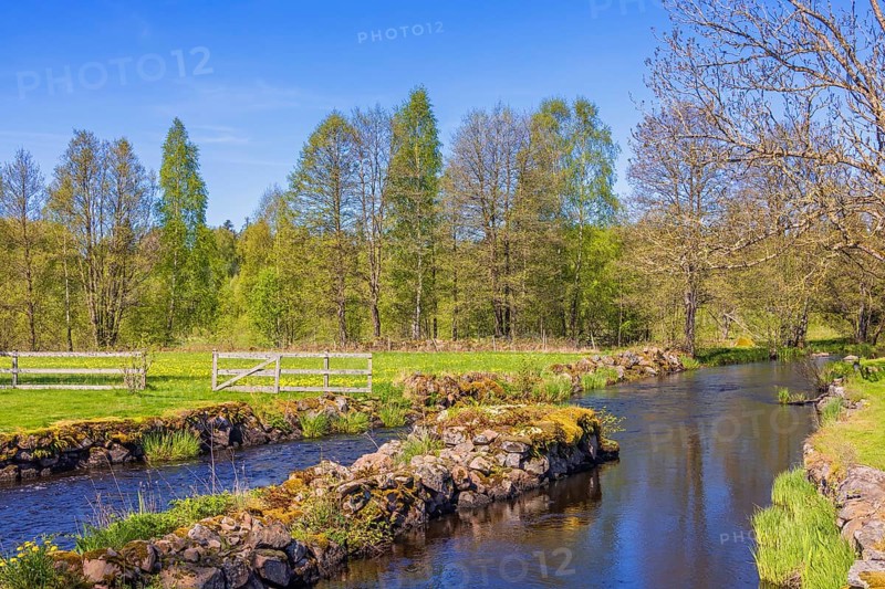 Water canal with stone piers in a beautiful rural landscape with green meadows and lush trees