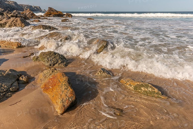 A rocky beach with a large rock in the foreground and a boat in the distance. The beach is quiet and peaceful, with the water. Camaret sur mer, Crozon, Finistere, Brittany, France, Europe
