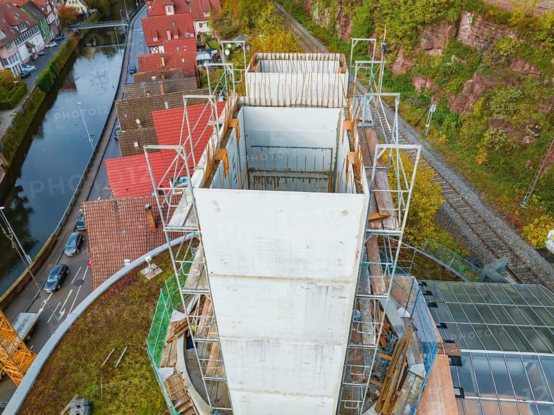 Construction site of a concrete tower next to a river with surrounding red houses and autumn trees, extension of the ZOB Calw tower on the new track of the Hermann Hesse railway, Calw, Black Forest, Germany, Europe