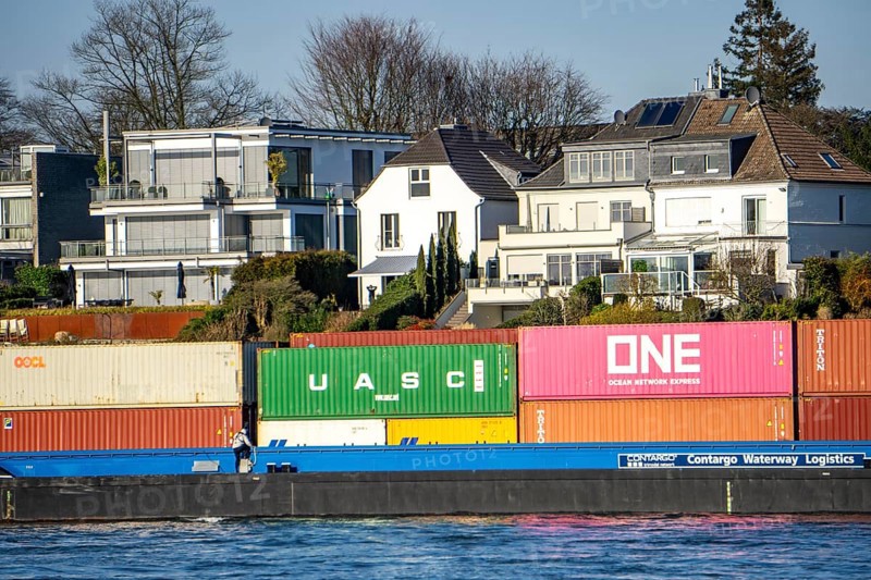 Container cargo ship on the Rhine near Düsseldorf-Bockum, villas on the banks of the Rhine, the neighbourhood in district 5 is one of the most expensive residential areas in Düsseldorf, North Rhine-Westphalia, Germany, Europe