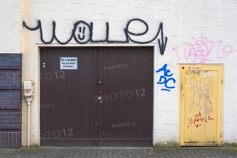 View of a graffiti-painted house facade with garage door and small entrance door, vandalism, street photography, Linden-Limmer, hannover, Nedersachsen, Germany, Europe