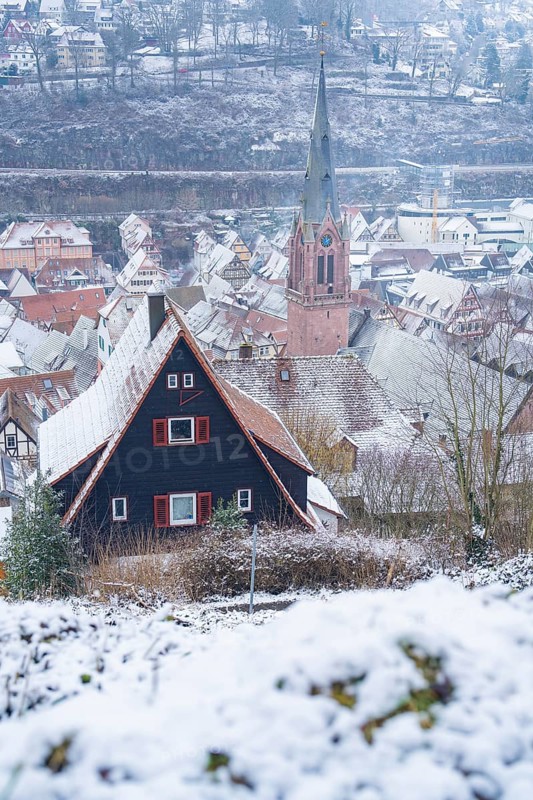 Winter village landscape with snow-covered roofs and striking church tower, New wooden footbridge in Calw town garden, Calw, Black Forest, Germany, Europe