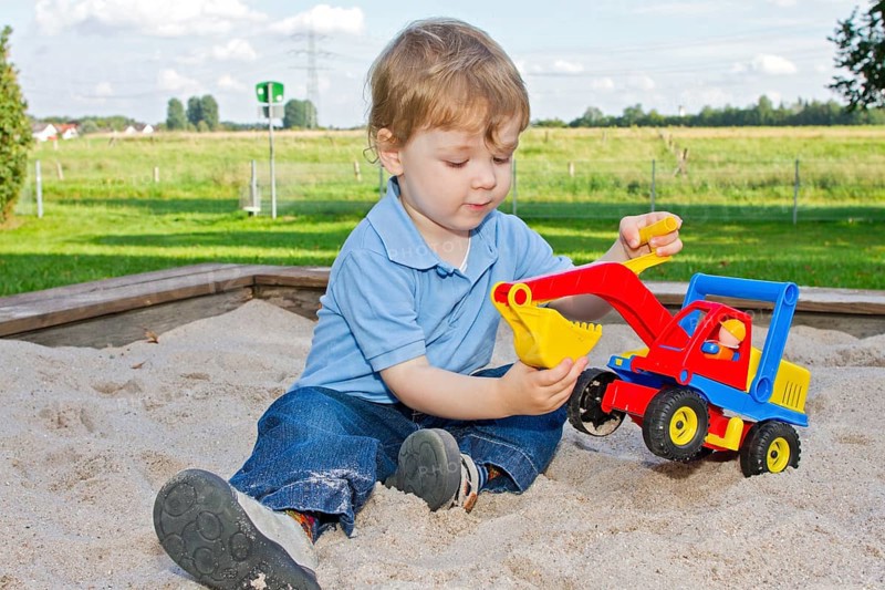 Three-year-old boy on the playground, sitting in the sandpit and playing with an excavator, toy, child, children