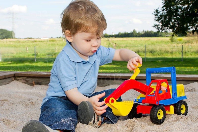 Three-year-old boy on the playground, sitting in the sandpit and playing with an excavator, toy, child, children
