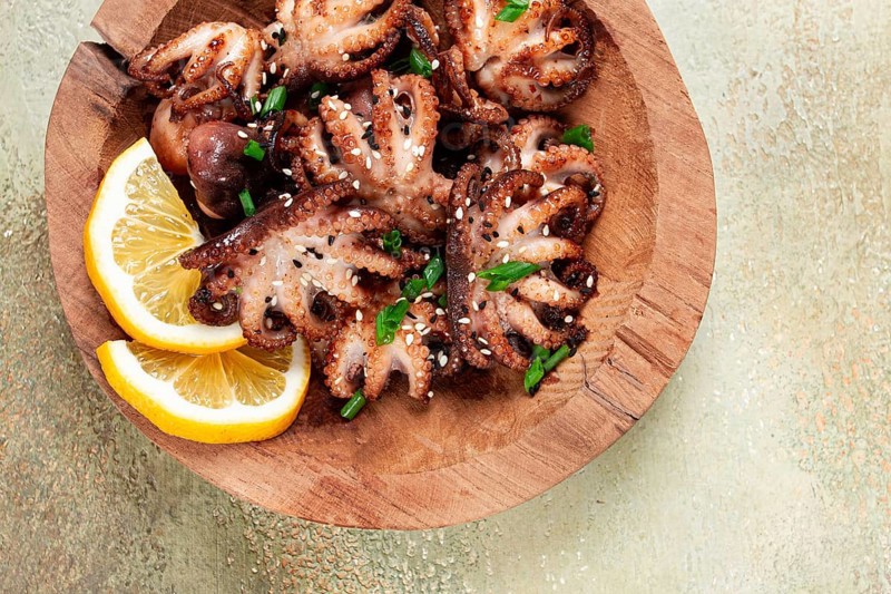 Grilled baby octopus with green onions, lemon slices, on a wooden plate, homemade, no people