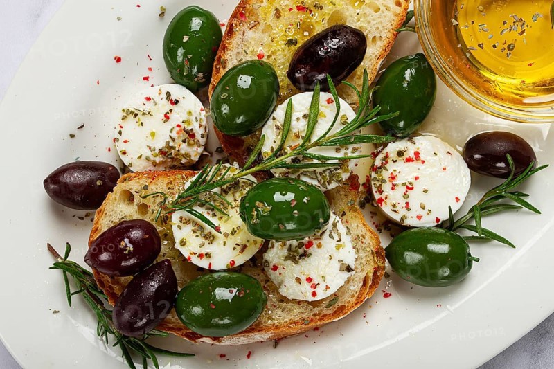 A plate with a snack, ciabatta bread with cheese and olives, olive oil, spices and herbs, top view, no people