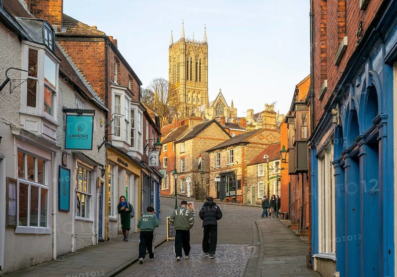 People walking up Steep Hill in evening light, cathedral tower rising above buildings, Lincoln, Lincolnshire, England, UK