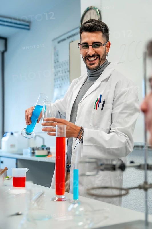 Young male scientist pouring blue liquid into laboratory glassware while smiling during an experiment in a university or school lab