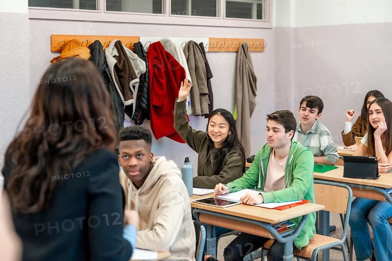 Multi ethnic group of high school students attending a lesson, a girl is raising her hand to ask a question to the teacher