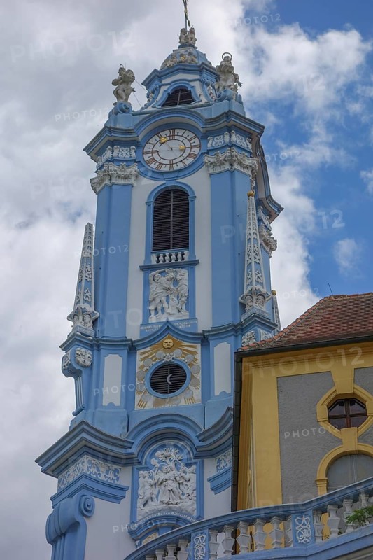 Baroque church tower with clock and richly decorated structures in blue and yellow, wachaus, donau, austria