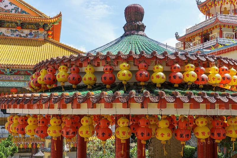 Richly decorated pavilion with hanging red and yellow lanterns. Temple in the background, penang, malaysia