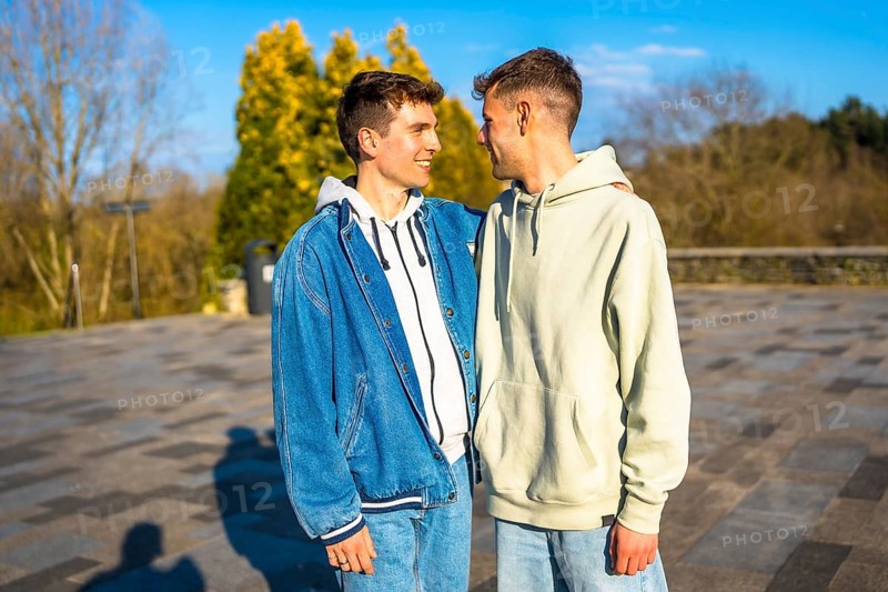 Two men embracing and smiling in a public park, sharing a joyful romantic moment together under the warm sunlight of a spring day