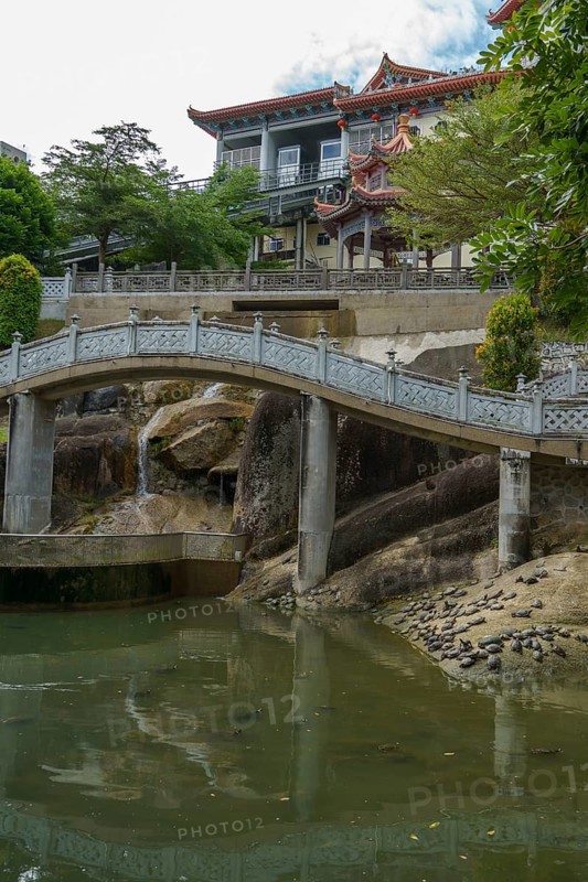 Stone bridge over pond leads to traditional temple complex, penang, malaysia
