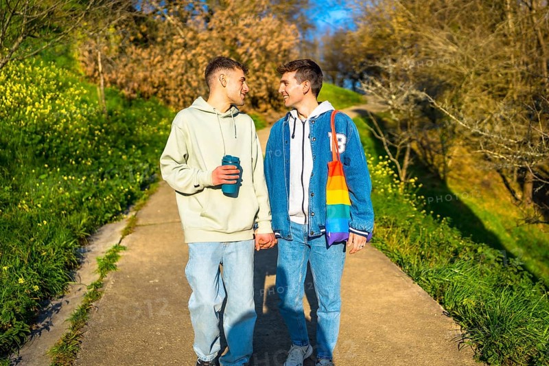 Young caucasian gay couple holding hands and walking in a park, enjoying a sunny day together