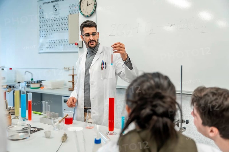 Chemistry teacher showing test tube with chemical reaction to students during experiment in university laboratory