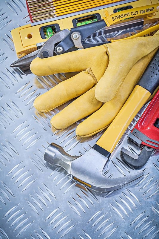 Composition of claw hammer leather safety gloves construction level wooden meter pliers pipe wrench on grooved metal plate