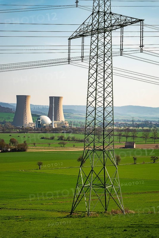 An electricity pylon stands in a green landscape with the Grohnde nuclear power plant in the background, Lower Saxony, Germany, Europe