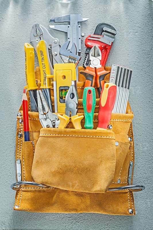 Assortment of construction tooling in tool belt on concrete background