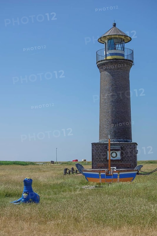 Brick lighthouse next to boat and blue sculpture in a meadow under blue sky, juist, north sea, germany