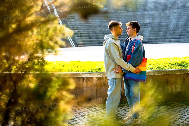 Two men embracing in a park, one showcasing a vibrant rainbow bag, celebrating lgbtq plus pride, love, and acceptance in a joyful moment