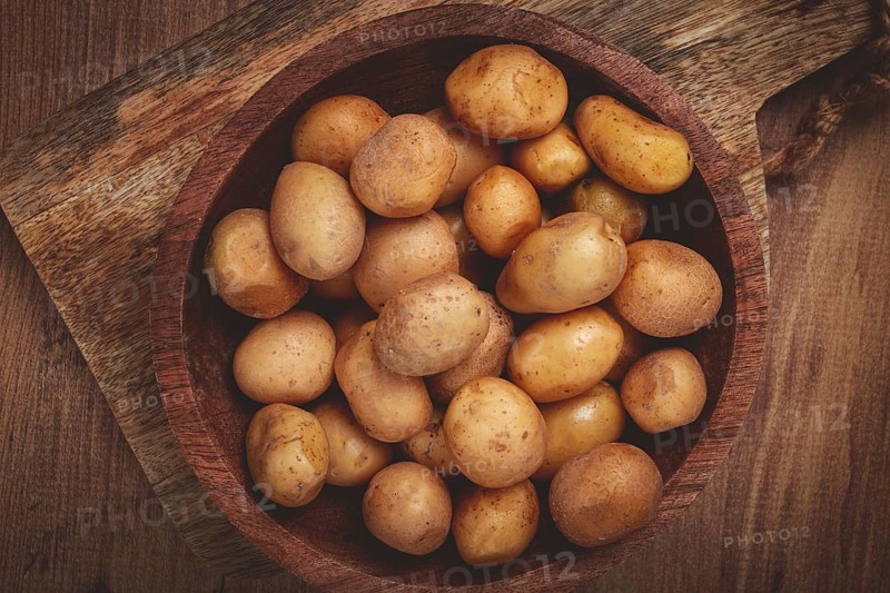 A bowl filled with freshly harvested small potatoes showcases their natural earthy tones. The wooden surface adds warmth and rustic charm to the setting.